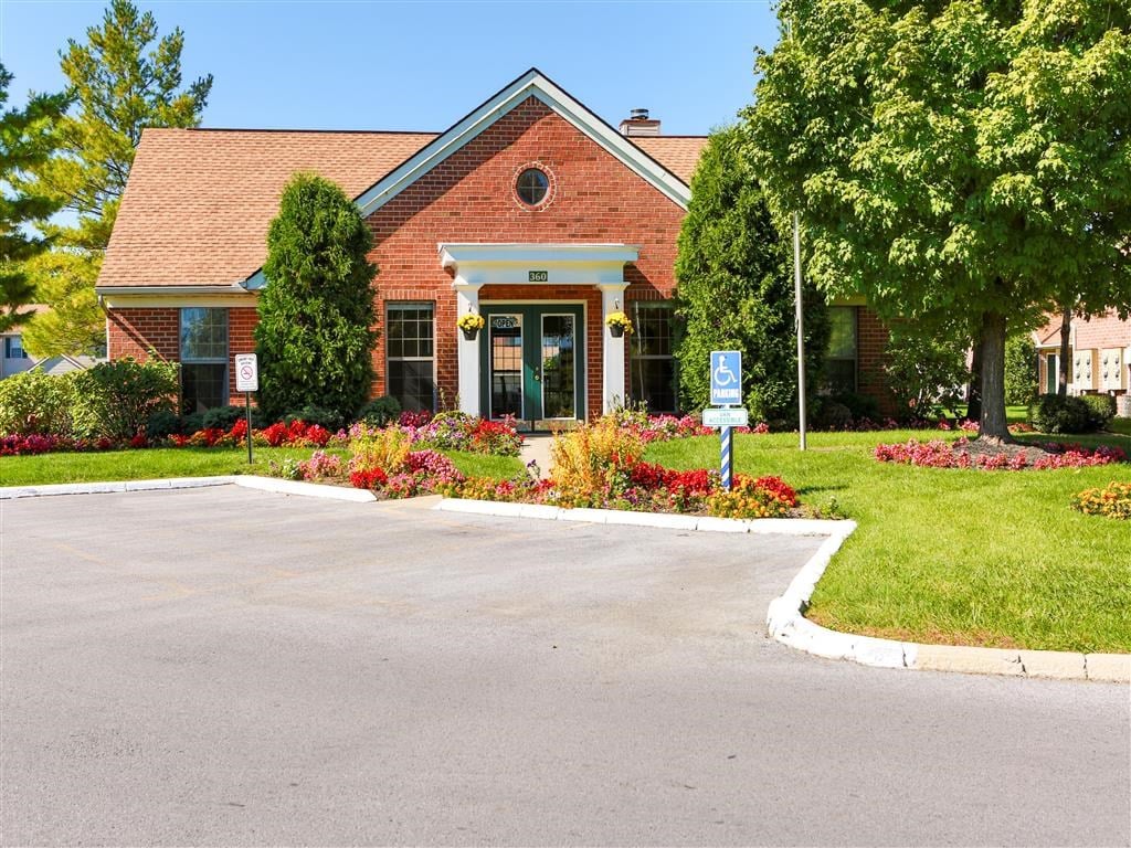 the front of a red brick house with a driveway and trees