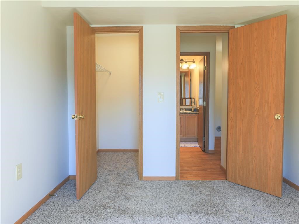 an empty bedroom with two doors and a hallway to a bathroom