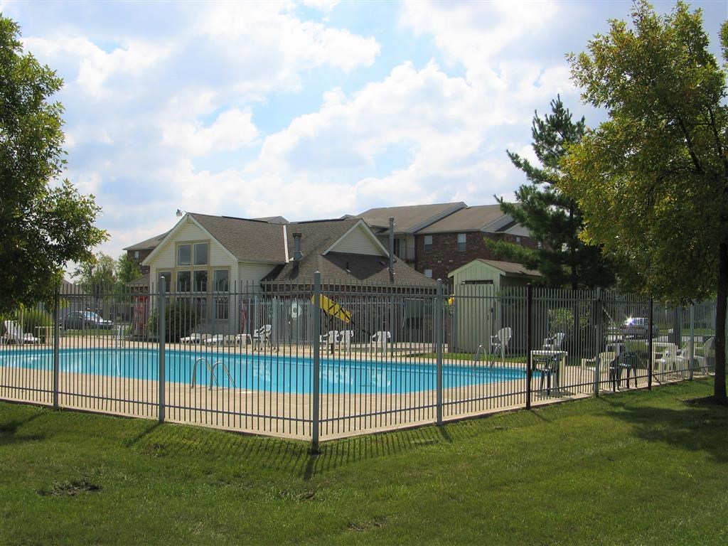 a swimming pool in front of a house behind a fence
