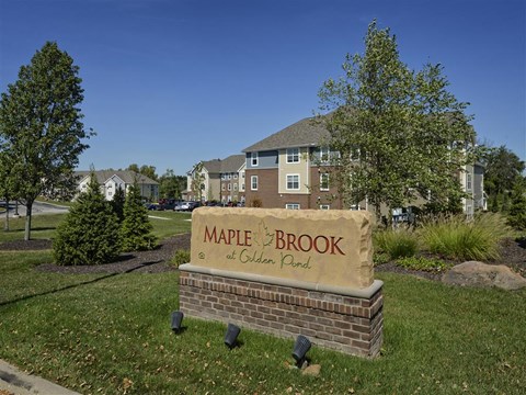 A sign for Maple Brook at Golden Plain in front of a building and trees.
