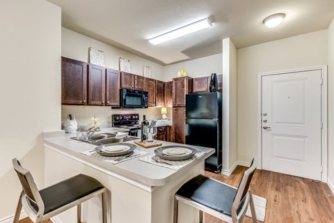 A kitchen with a table set for two with a black fridge and microwave.