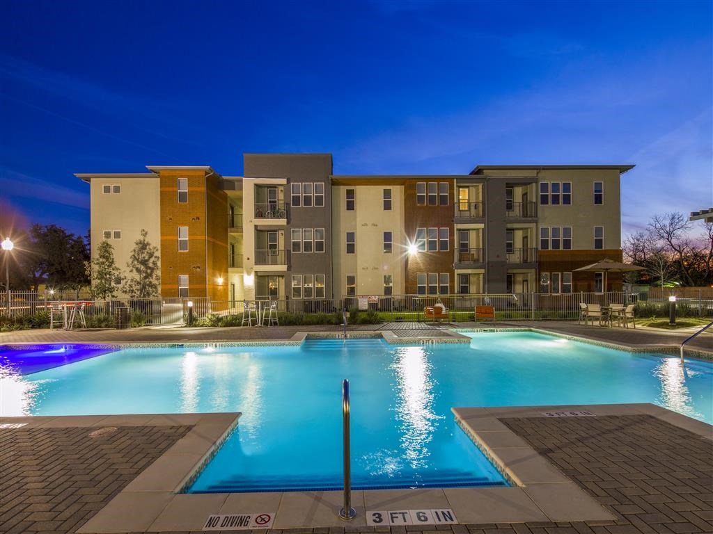 a swimming pool at night with an apartment building in the background