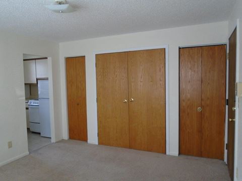 an empty living room with three doors and a kitchen