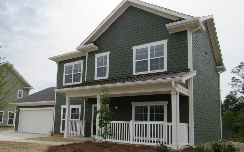 a green house with a porch and a white fence