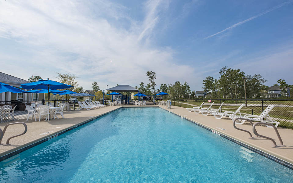 our resort style swimming pool is surrounded by lounge chairs and umbrellas