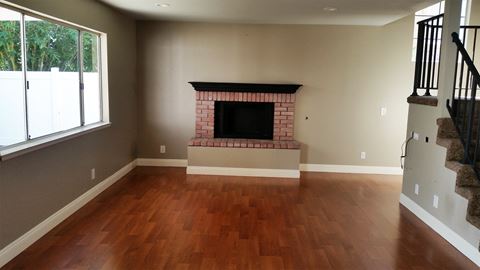 an empty living room with a brick fireplace and wooden floors