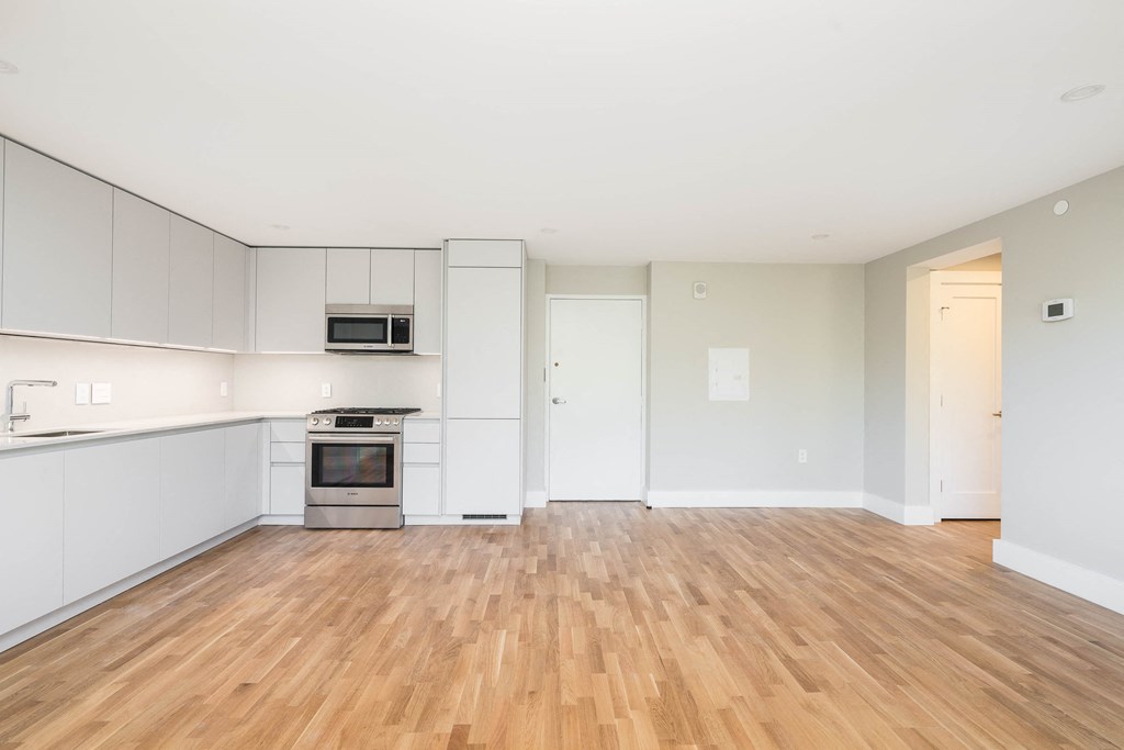 an empty kitchen with white cabinets and a wooden floor