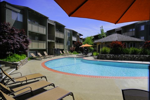 a large pool with chairs and umbrellas in front of an apartment building
