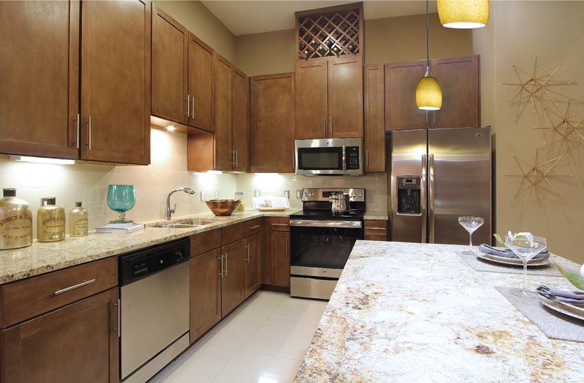 Luxury apartments with spacious kitchen and built-in wine rack, granite countertops, kitchen island, stainless steel appliances, and designer tile backsplash at Tuscany Walk Apartments in Houston Texas.