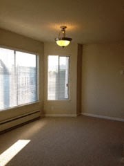 an empty living room with a large window and a ceiling light