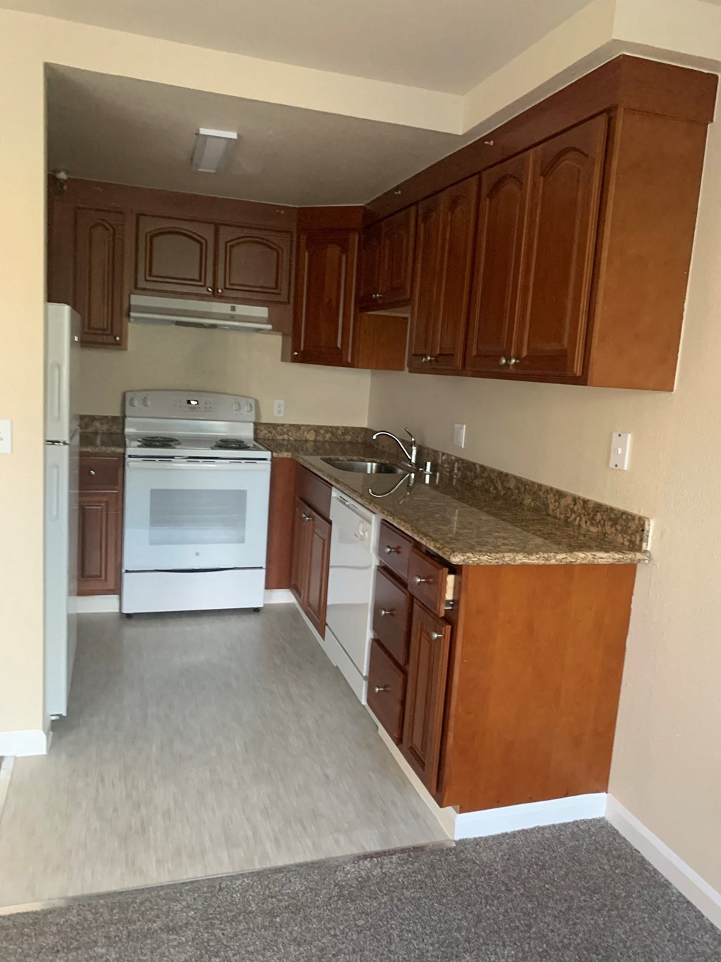 an empty kitchen with white appliances and granite counter tops