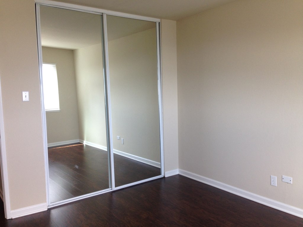an empty room with a wood floor and mirrored closet doors