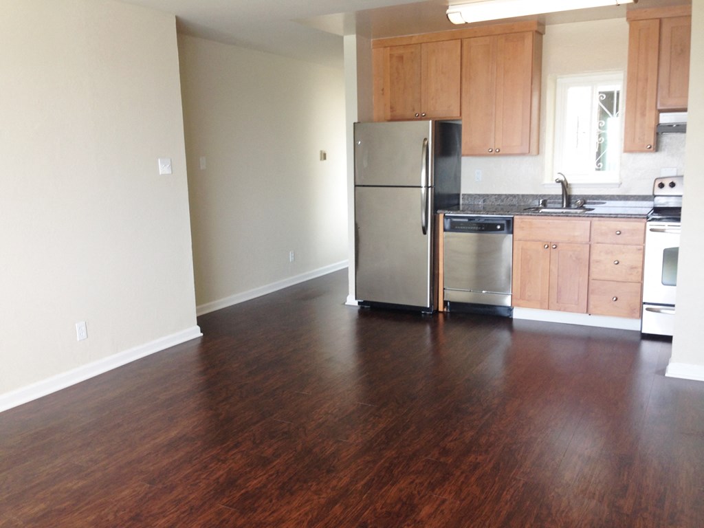 an empty kitchen with wooden floors and a stainless steel refrigerator