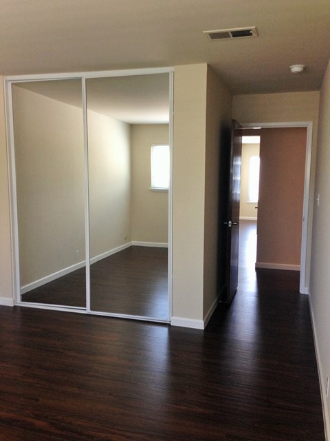 an empty living room with a hard wood floor and mirrored closet doors