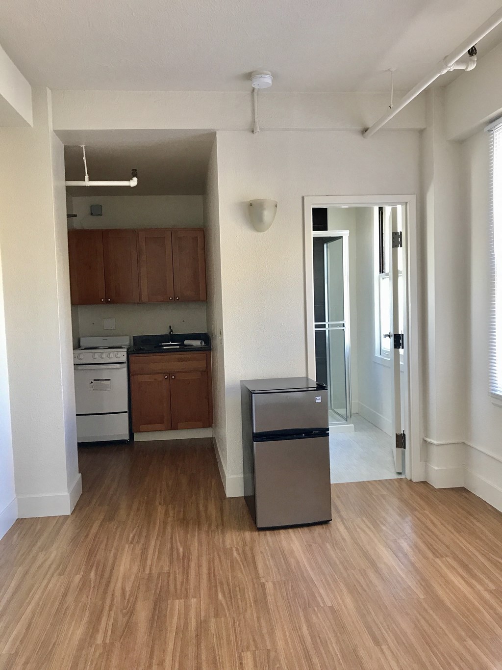 an empty living room with a refrigerator and a kitchen