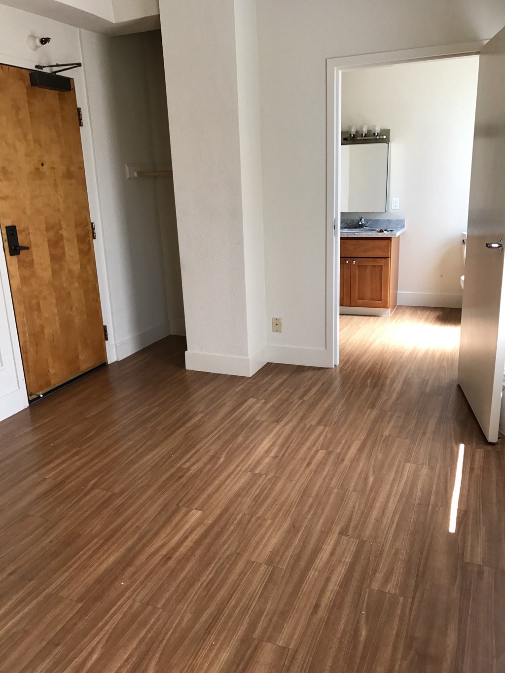 an empty living room with wooden floors and a door to a kitchen