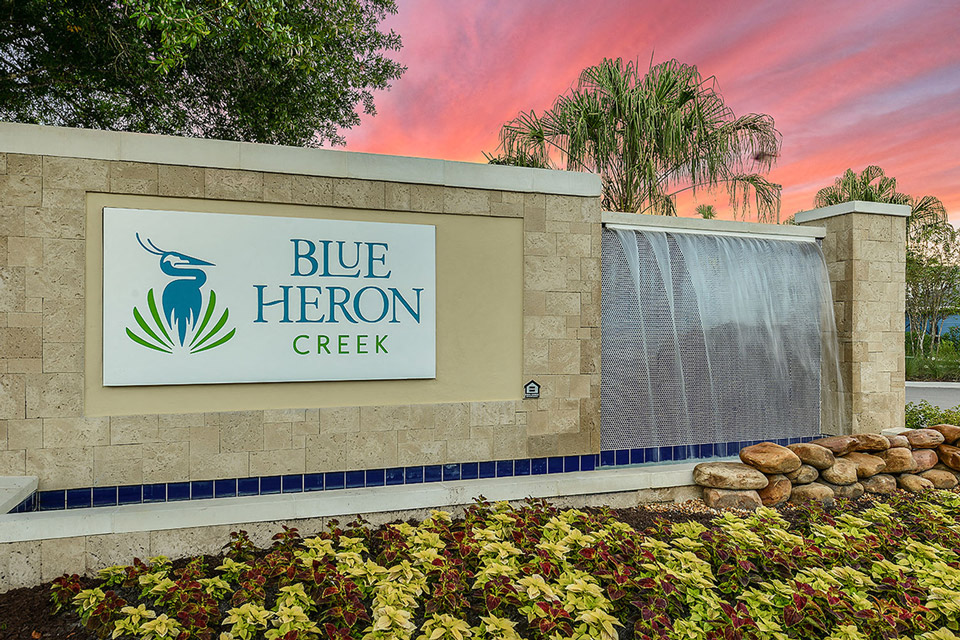 a sign for blue heron creek at sunset in front of a waterfall