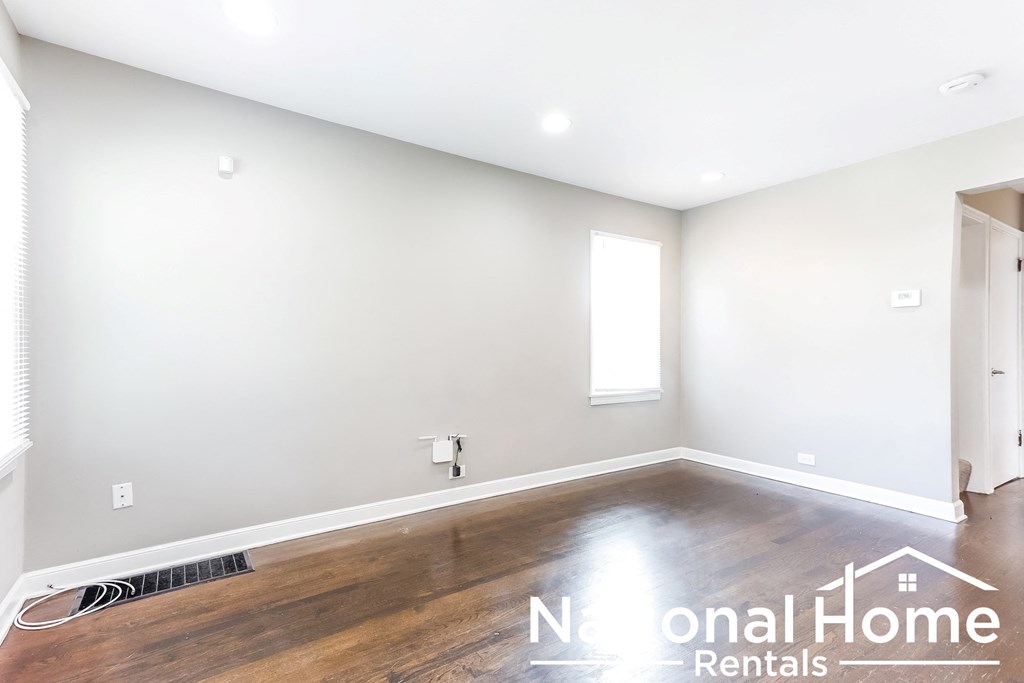 A spacious room with wooden floors and white walls, with a window and a door visible.