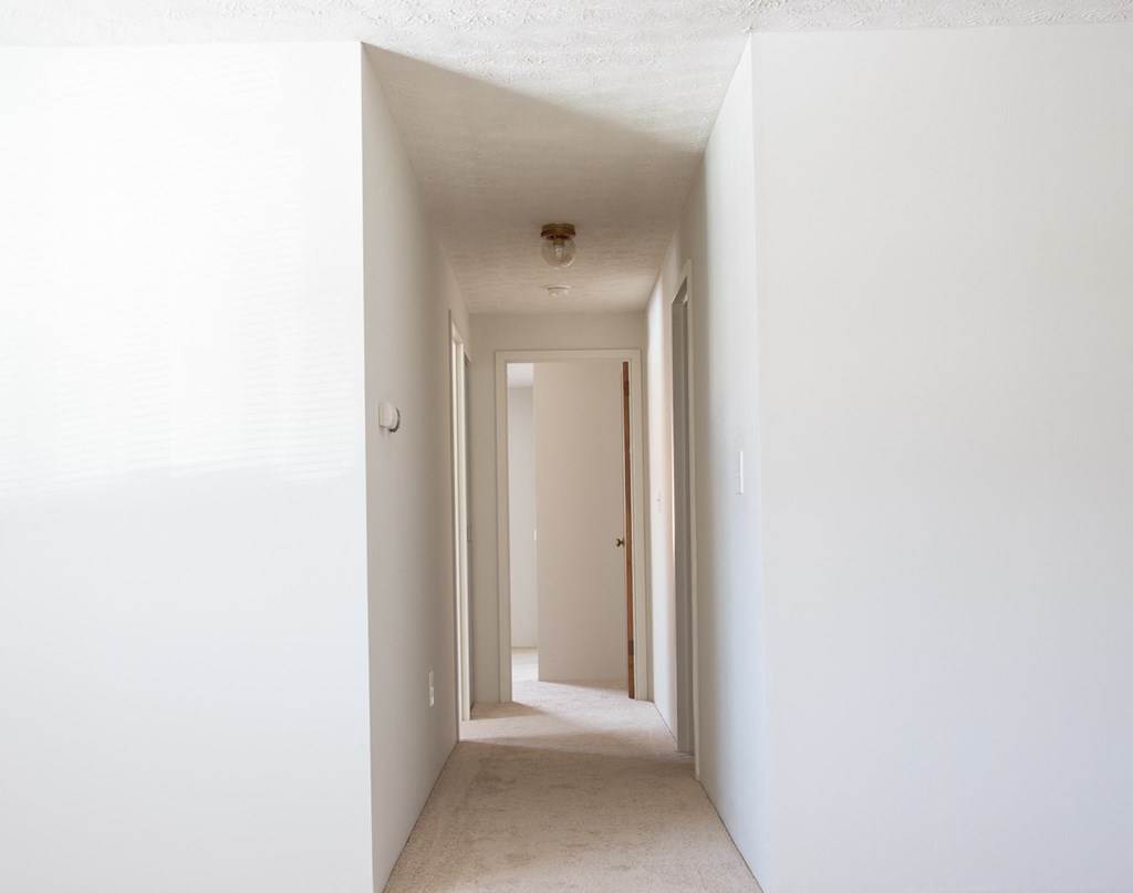 an empty hallway with white walls and a ceiling light