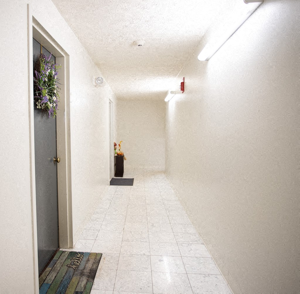 a long white hallway with a door and a vase of flowers