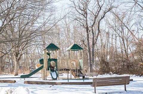 a playground with two swings and a bench in the snow