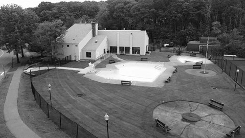 A black and white image of a park with a playground and a building in the background.