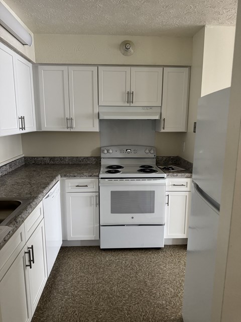 A kitchen with white cabinets and a white stove top oven.