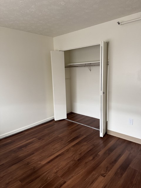 A room with a white wall and a brown floor with a closet.