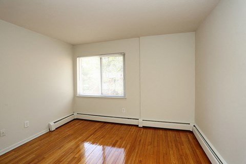 a bedroom with white walls and wood floors and a window