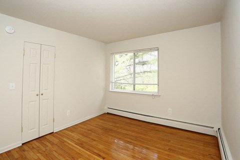 a bedroom with white walls and wood floors and a window