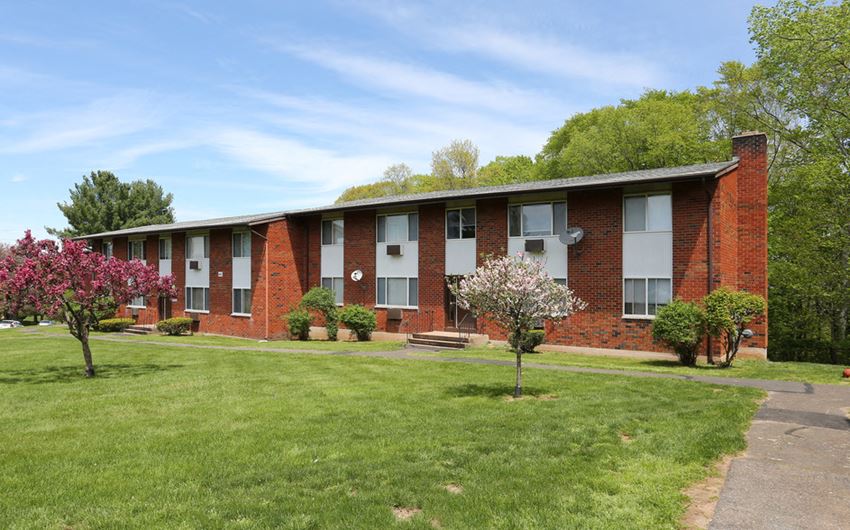 a red brick apartment building with green grass and flowering trees