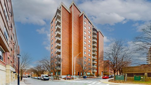 A tall red brick building with a parking lot in front.