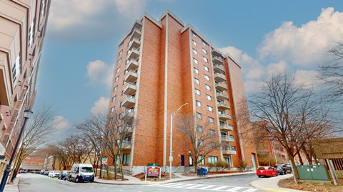 A tall red brick building with a parking lot in front.