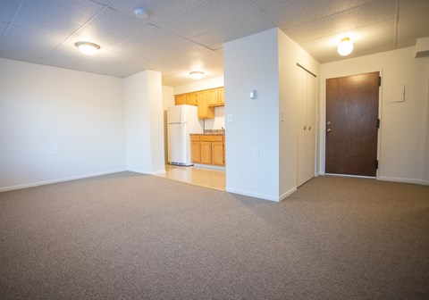 an empty living room with a kitchen in the background