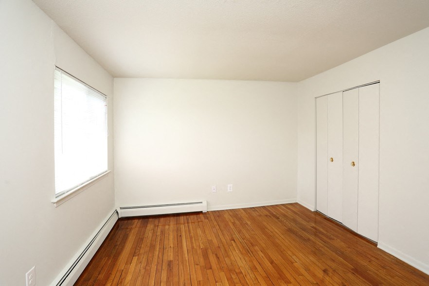 a bedroom with white walls and wood floors and a window