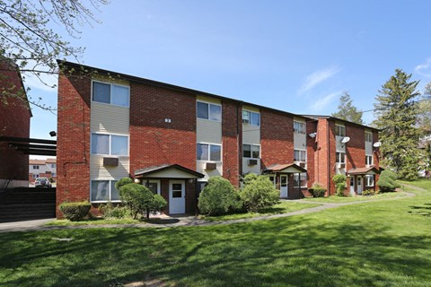 exterior view of a brick apartment building with green grass and trees