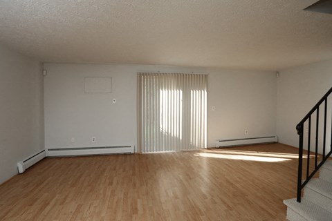 the living room and dining room of an apartment with wood flooring and a staircase
