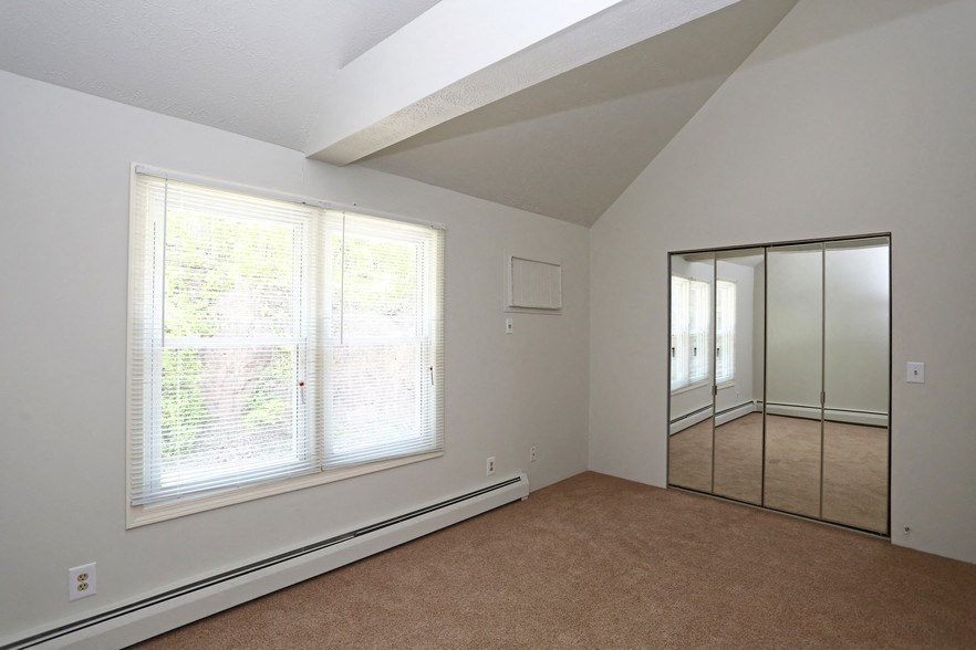 an empty bedroom with a large window and a mirrored closet