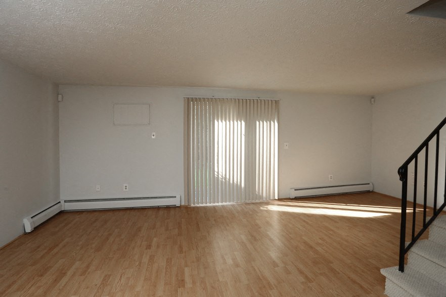 the living room and dining room of an apartment with wood flooring and white walls