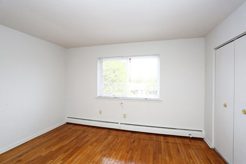 a bedroom with white walls and a window and wooden floors