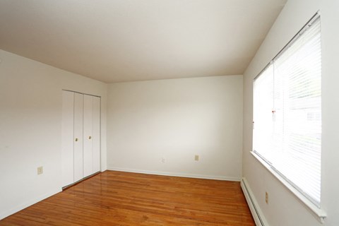 a bedroom with white walls and wood floors and a large window