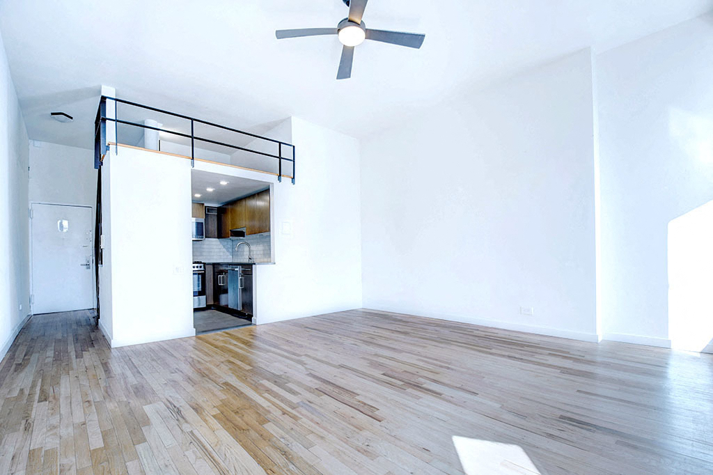an empty living room with a ceiling fan and a kitchen