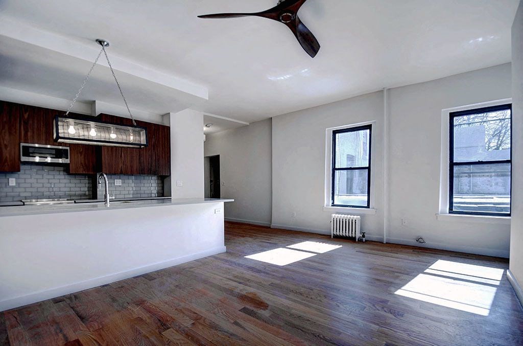 an empty living room with a kitchen and a ceiling fan