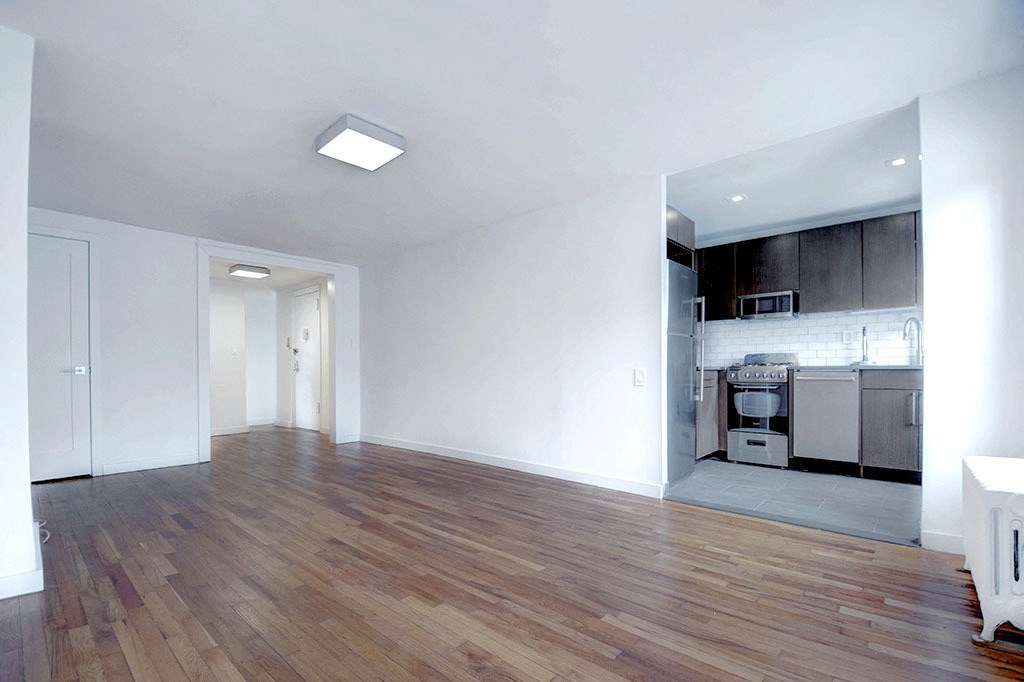 an empty living room with a kitchen in the background