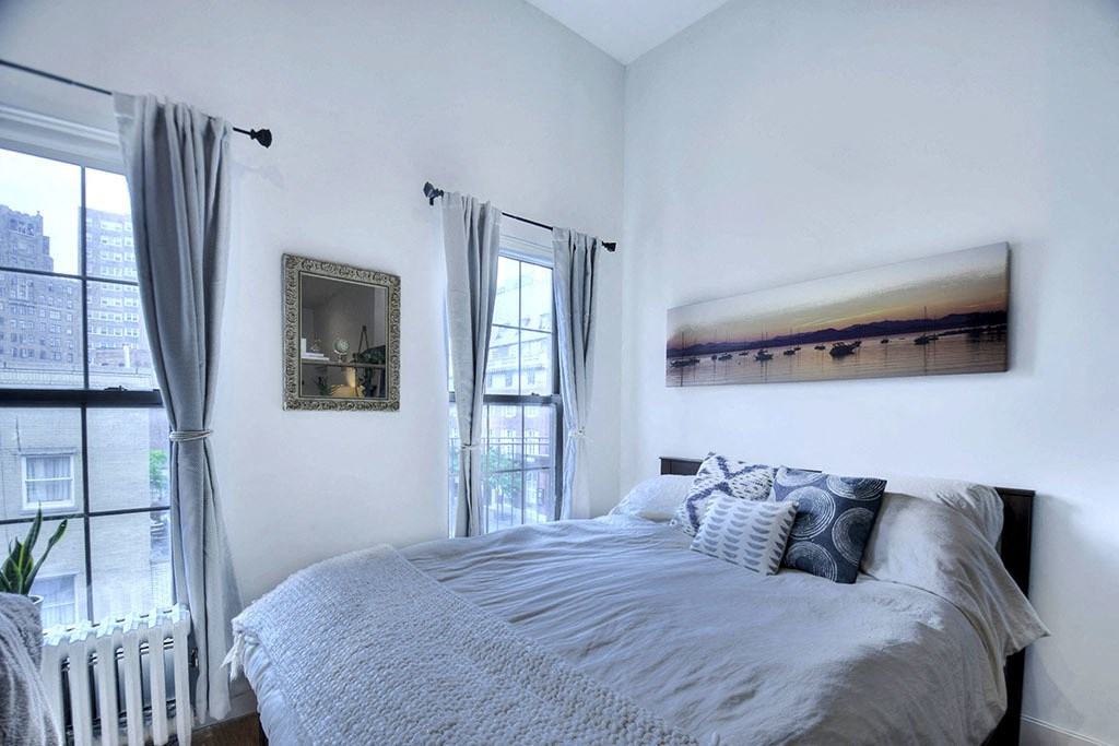 a bedroom with a bed and two windows and a painting on the wall