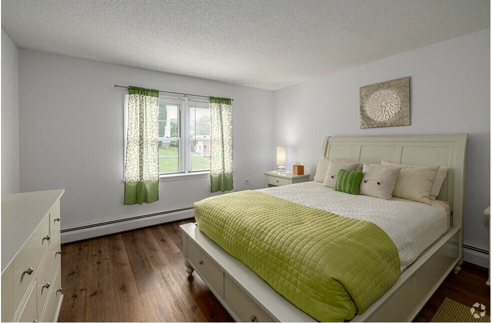 A bedroom with a white bed and green bedspread.
