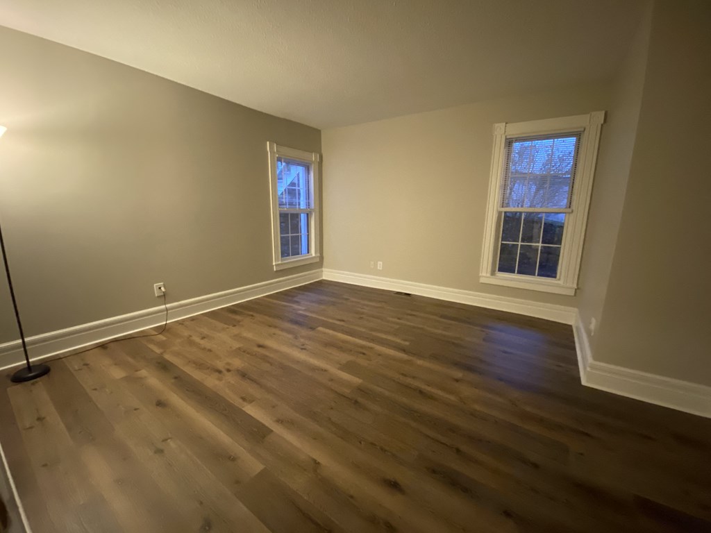 an empty living room with wooden floors and two windows