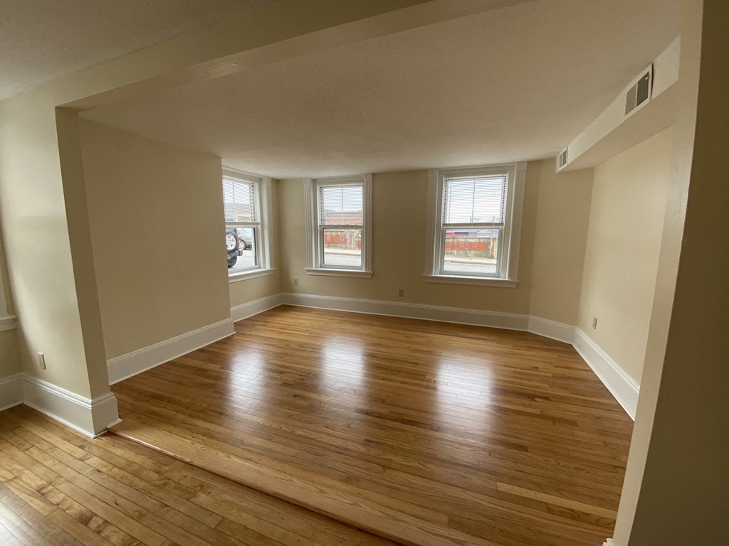 an empty living room with wooden floors and three windows