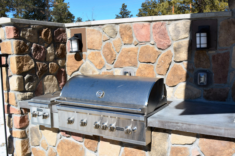 a stainless steel barbecue grill in front of a stone wall