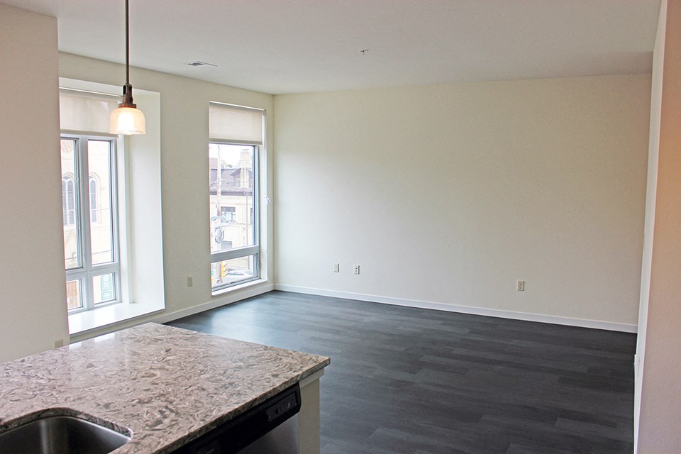 an empty living room with a kitchen counter and a window
